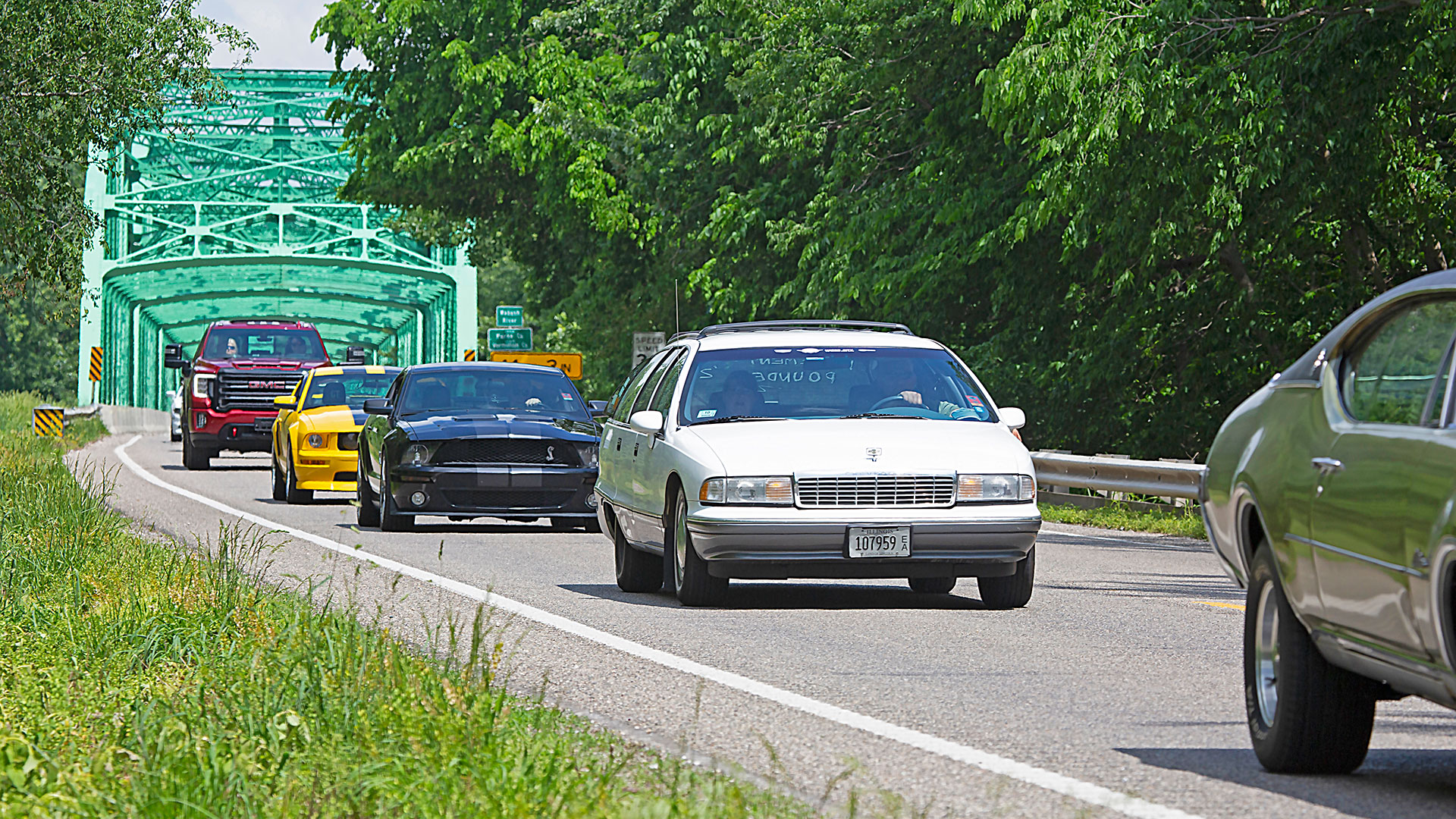 Classic cars driving american backroads with steel bridge in background